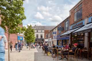 After shot of Altrincham after public realm works have been completed, complete with street trees and new paving setts. People are sat outside cafes and bars spilling out on to the street.