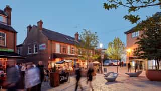 A small courtyard in Altrincham at dusk. Local bars and restaurants have spill out outdoor seating as people pass through the courtyard.