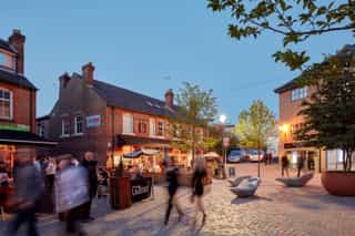 A small courtyard in Altrincham at dusk. Local bars and restaurants have spill out outdoor seating as people pass through the courtyard.