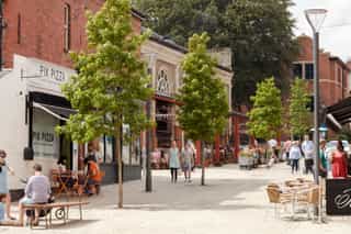 Complete image of Altrincham town centre showing new paving setts and sreet trees. Cafe and bars have spill out seating.