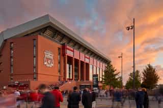 An image of Anfield Stadium at sunset, with fans walking around