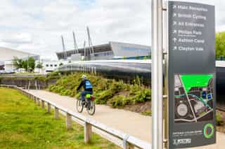 An image of a man cycling on a path outside the Velopark, with a wayfinding sign to the left of the image