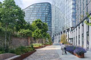 A cyclist meandering through Angel Meadow, surrounded by green and purple planting within corten planters and the Coop building in the distance.