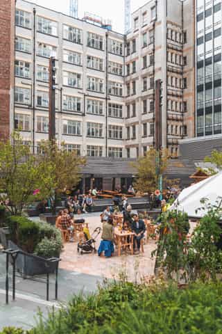 Image showing Sadler's yard nestled between the surrounding buildings, people are sat enjoying themselves alongside plating and the Pilcrow pub.