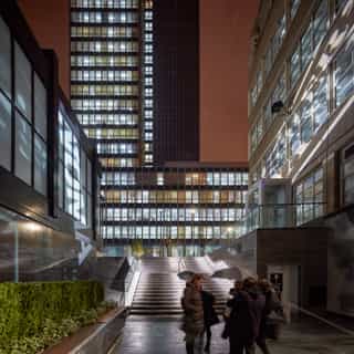 Twilight shot of Sadler's Yard. Surrounding buildings are alight, with people walking towards the illuminated steps into the yard.