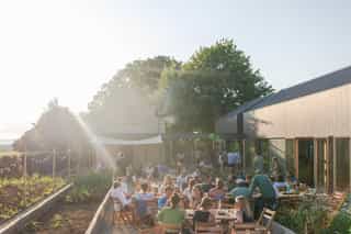 An image of people gathered outside sitting down at long tables, a ray of light shines down from the top left corner