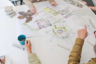 An high angle view image of colourful plan designs, with hands gesturing, one holding a mug
