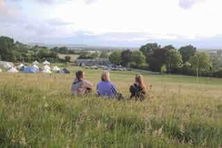 An image of people sitting in long grass looking down towards the Gloucestershire studio
