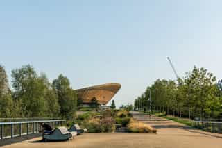 An image of the Queen Elizabeth Olympic Park in the distance, showing the pathway and planting, the seating is in use.