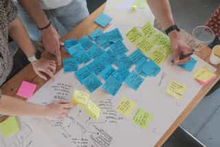 Image showing hands taking notes, and colourful post it notes during a workshop.