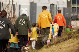 An image of people wearing different coloured jackets with the PLANT logo on the back, they are walking along a narrow path with kids